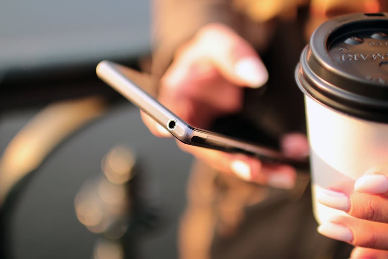 Person checking their phone while holding a coffee